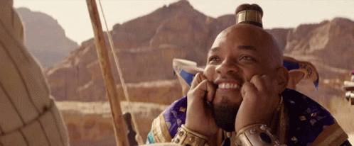A Man With A Crown On His Head Is Smiling With His Hands On His Chin GIF