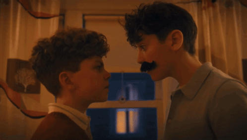 a man with a fake mustache touches the nose of another man