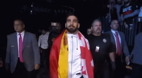 A Man With A Flag Around His Neck Walks Through A Crowd GIF