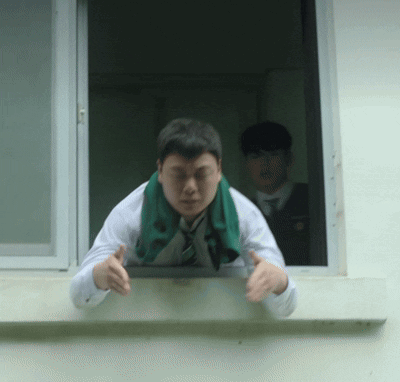 A Man With A Green Scarf Around His Neck Leans Out Of A Window GIF