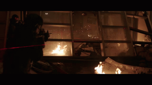 A Man With A Gun Is Standing In Front Of A Window With A Fire Coming Out Of It GIF