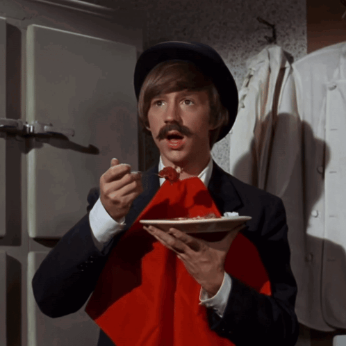 A Man With A Hat And Mustache Holds A Plate Of Food GIF
