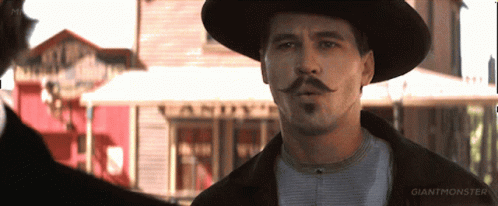 A Man With A Hat And Mustache Is Standing In Front Of A Building That Says Giant Monster GIF