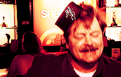 A Man With A Hat On His Head Is Sitting In Front Of A Sign That Says Sna GIF