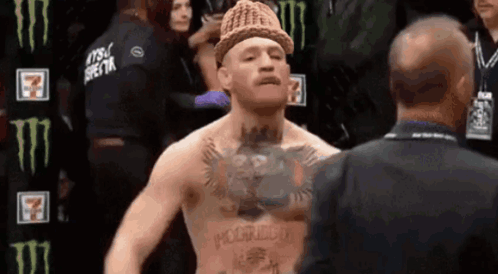 A Man With A Hat On His Head Is Talking To Another Man In A Suit . GIF