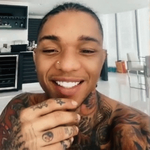 A Man With A Lot Of Tattoos On His Arms And Neck Is Smiling . GIF