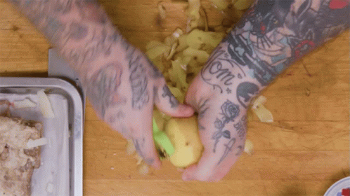 A Man With A Lot Of Tattoos On His Arms Is Peeling A Potato GIF