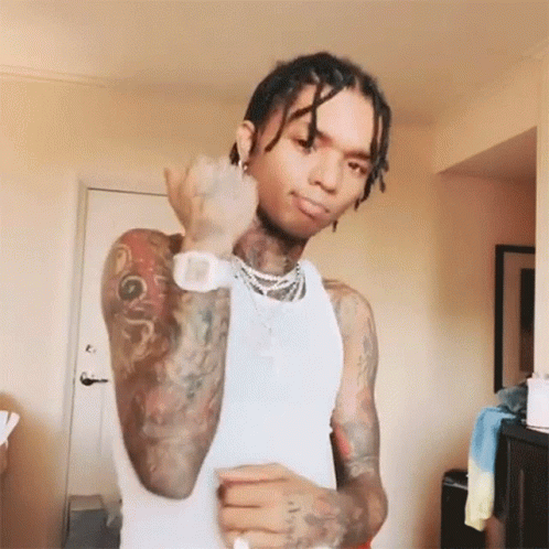 A Man With A Lot Of Tattoos On His Body Is Wearing A White Tank Top And A Watch . GIF