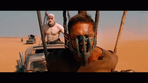 A Man With A Mask On His Face Is Driving A Car In The Desert GIF