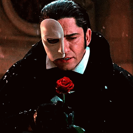 A Man With A Mask On His Face Is Holding A Rose . GIF