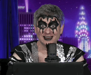 A Man With A Mask On His Face Is Sitting In Front Of A Microphone With A Building In The Background That Has The Word Do GIF
