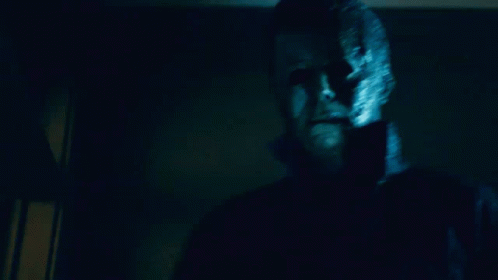 a man with a mask on his face is standing in a dark room looking at the camera