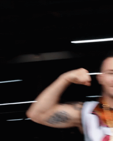 A Man With A Medal Around His Neck Flexes His Arm GIF