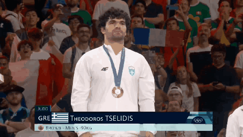 A Man With A Medal Around His Neck Is Standing In Front Of A Crowd GIF