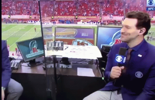 A Man With A Microphone Sitting In Front Of A Screen That Says Champions On It GIF