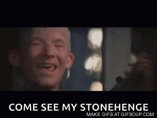 A Man With A Missing Tooth Is Laughing In Front Of A Mirror With The Words `` Come See My Stonehenge '' Below Him . GIF