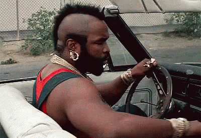 A Man With A Mohawk Is Driving A Car With His Hand On The Steering Wheel GIF