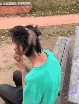 A Man With A Mohawk On His Head Sits On A Wooden Bench GIF
