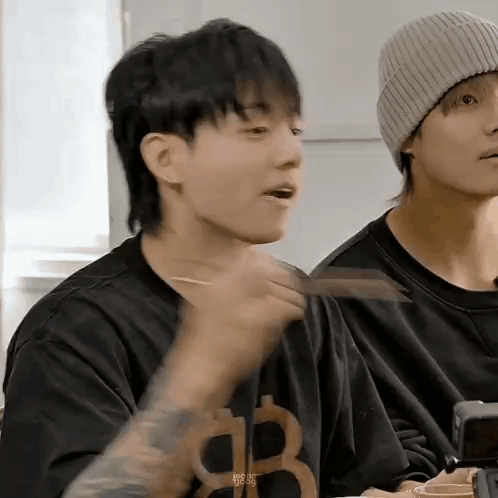 A Man With A Mullet Is Eating Food With Chopsticks While Sitting At A Table . GIF