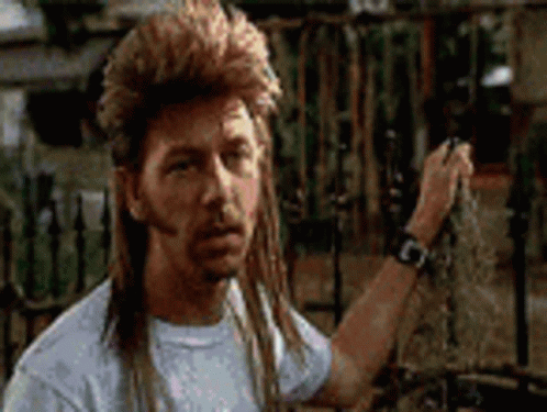 A Man With A Mullet Is Standing In Front Of A Fence Holding A Chain . GIF