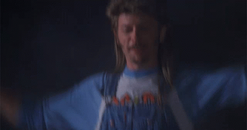 A Man With A Mullet Wearing A Blue Shirt That Says ' Mountain ' On It GIF