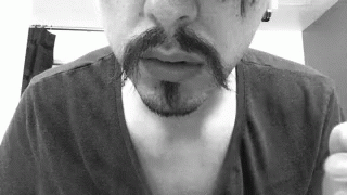 A Man With A Mustache And A Beard Is Wearing A Black Shirt In A Black And White Photo . GIF