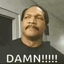 A Man With A Mustache And A Black Shirt Is Standing In Front Of A Door And Says `` Damn !!! '' . GIF