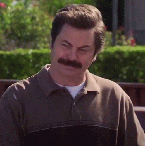 A Man With A Mustache And A Brown Shirt Looks At The Camera GIF