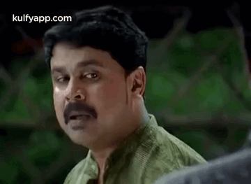 A Man With A Mustache And A Green Shirt Is Making A Funny Face . GIF