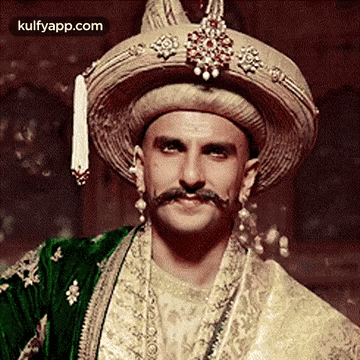 A Man With A Mustache And A Hat Is Wearing A Traditional Indian Outfit . GIF