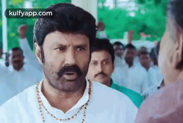 A Man With A Mustache And A Necklace Is Talking To Another Man In A Crowd Of People . GIF