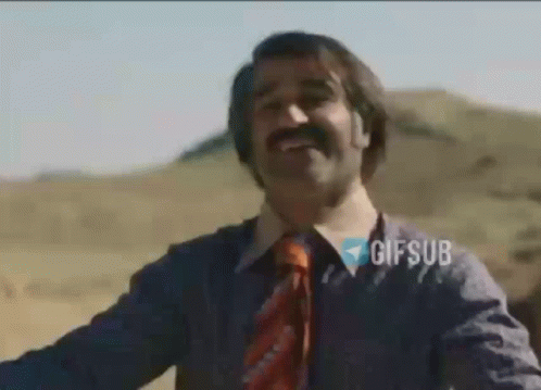A Man With A Mustache And A Tie Is Smiling While Standing In The Desert . GIF
