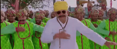 A Man With A Mustache And Sunglasses Is Dancing In Front Of A Crowd Of Men Wearing Green Clothes And Hats . GIF