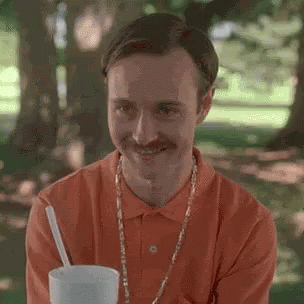 A Man With A Mustache Is Drinking A Milkshake In A Park . GIF