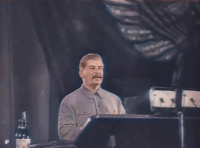 A Man With A Mustache Is Giving A Speech On A Stage GIF