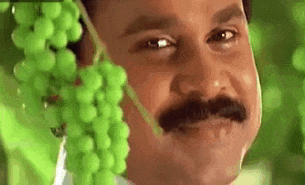 A Man With A Mustache Is Holding A Bunch Of Grapes Over His Face . GIF