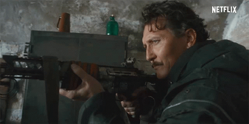 Man With Mustache Holding Rifle In Front Of Netflix Sign GIF