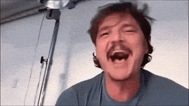 a man with a mustache is laughing while wearing a blue shirt