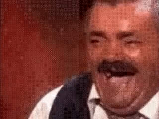 A Man With A Mustache Is Laughing With His Tongue Out While Wearing A Vest And Tie . GIF