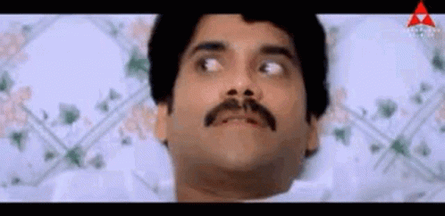A Man With A Mustache Is Laying In Bed With His Eyes Closed And Making A Funny Face . GIF