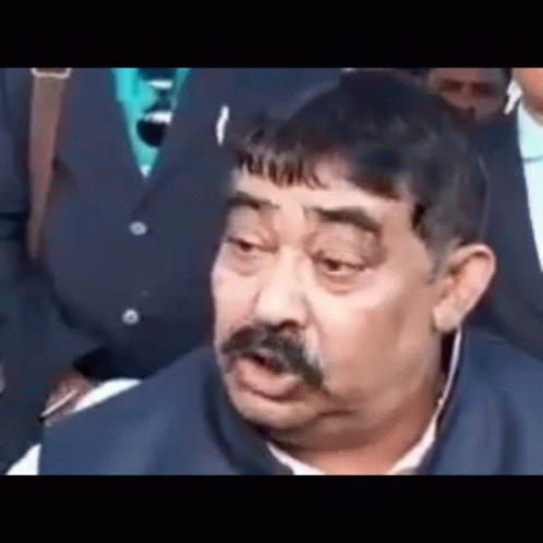 a man with a mustache is making a funny face while sitting in front of a group of people .