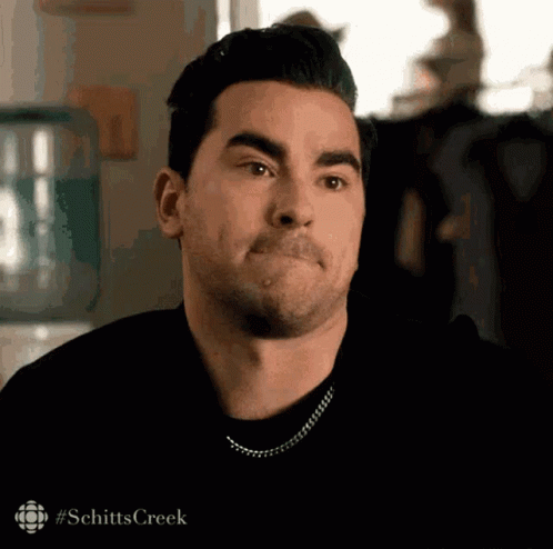 A Man With A Mustache Is Making A Funny Face While Wearing A Black Shirt And A Chain Around His Neck . GIF
