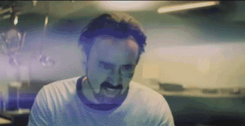 A Man With A Mustache Is Making A Funny Face While Wearing A White Shirt . GIF