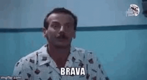 A Man With A Mustache Is Pointing At The Camera While Wearing A Shirt That Says Brava . GIF