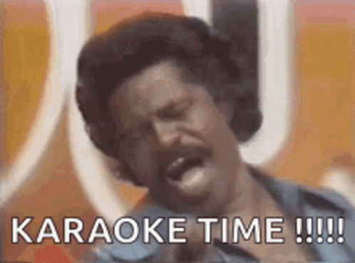 a man with a mustache is singing into a microphone with the words `` karaoke time !!! '' written below him .