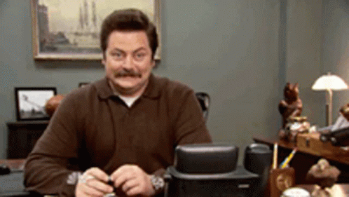 A Man With A Mustache Is Sitting At A Desk GIF