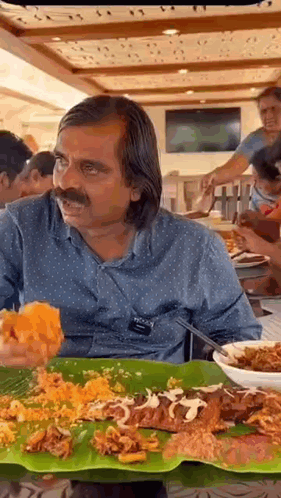 A Man With A Mustache Is Sitting At A Table Eating A Lot Of Food . GIF
