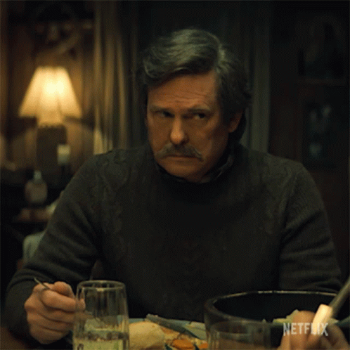 A Man With A Mustache Is Sitting At A Table With A Netflix Logo On The Bottom Right GIF