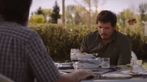 A Man With A Mustache Is Sitting At A Table With Plates And Glasses Of Wine . GIF