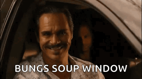 A Man With A Mustache Is Sitting In A Car With The Words Bungs Soup Window Written On The Screen Behind Him . GIF